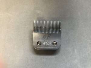 Metal pet grooming clipper blade on gray surface.